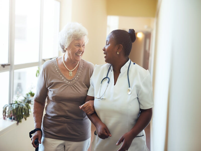 A nurse and a woman walking together and smiling at each other